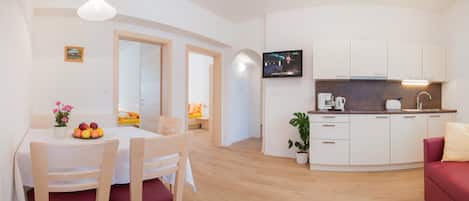 Una sala de estar moderna con comedor, cocina y televisor montado en la pared.