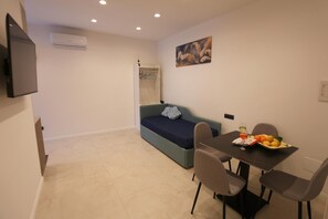 Ein gemütlicher Wohnbereich mit Sofa, Esstisch mit Stühlen, Fernseher und Wandklimaanlage.