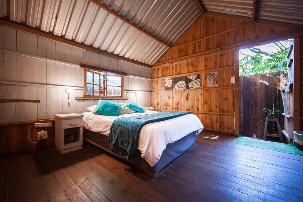 Un dormitori de cabana de fusta amb llit, taulella de nit i finestra.