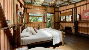 Une cabane en bois rustique, avec un lit simple, une petite table et une fenêtre donnant sur un paysage verdoyant.