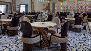 Une salle de banquet spacieuse, dotée de tables rondes, de chaises rembourrées et d’un plafond décoratif.