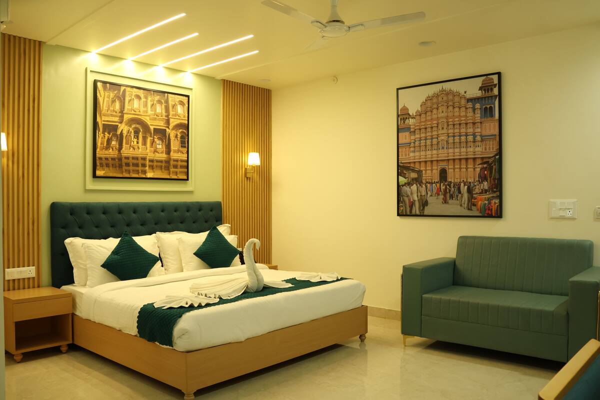Une chambre d’hôtel avec un grand lit, un canapé vert et deux lampes fixées au mur.