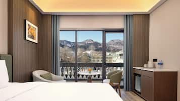 Ein Hotelzimmer mit Bett, Schreibtisch, Stuhl, Tisch und Balkon mit Blick auf die Berge.