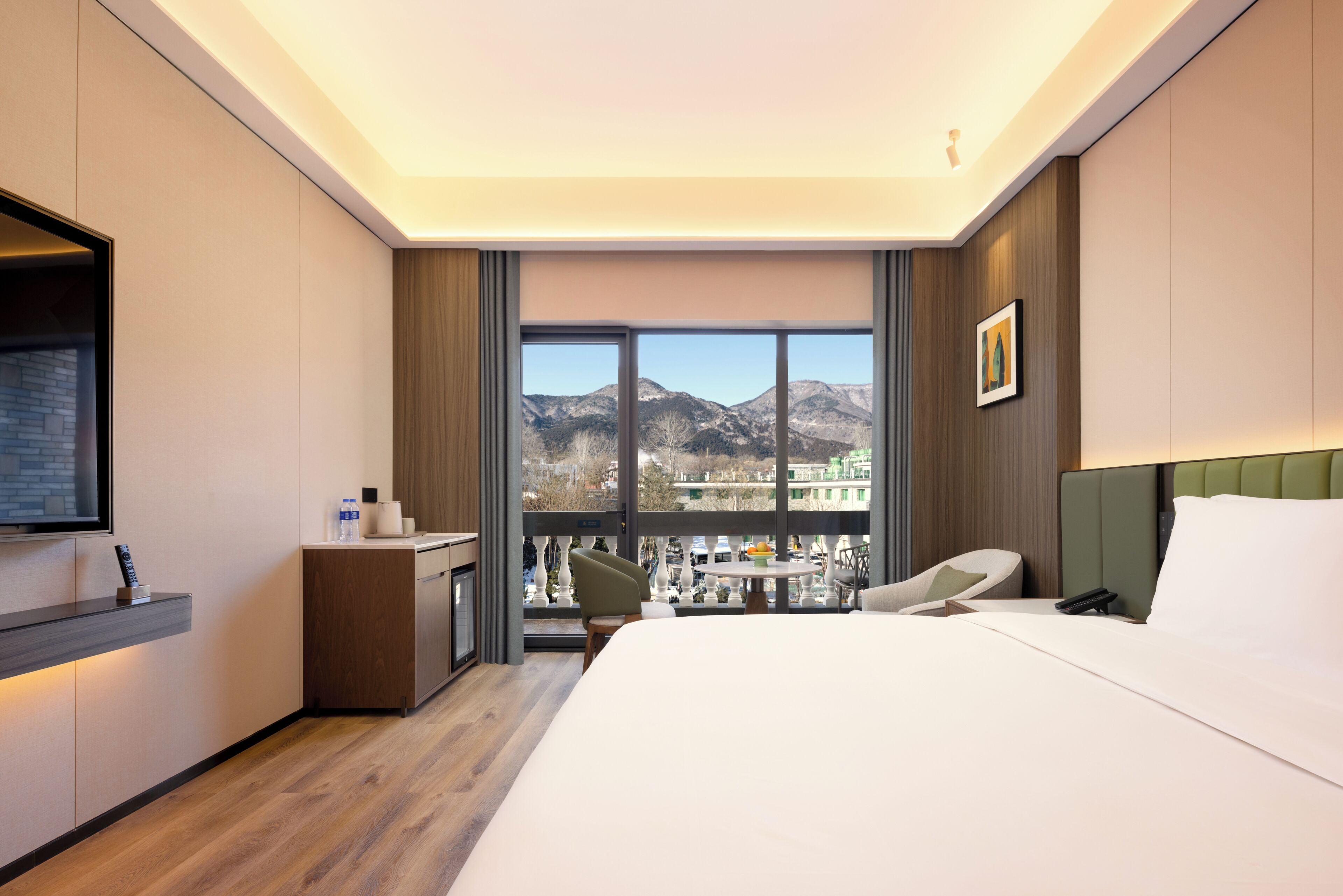 A hotel room with a bed, a desk, a chair, a TV, and a view of mountains.