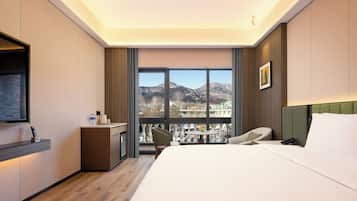 A hotel room with a bed, a desk, a chair, a TV, and a view of mountains.