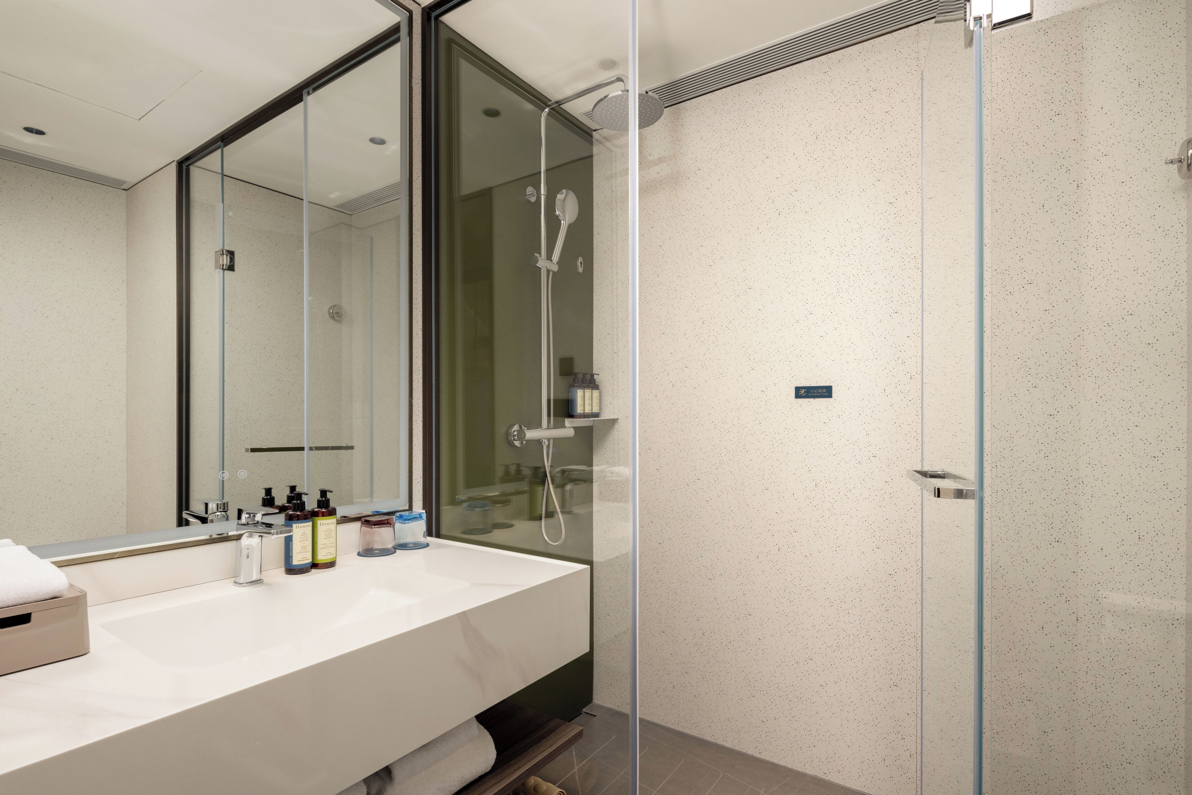 Un baño moderno con cabina de ducha de vidrio, un espejo grande y una encimera blanca con artículos de aseo.
