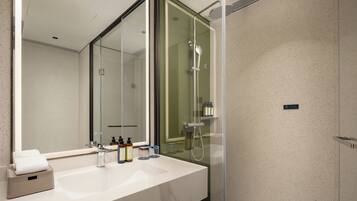 A modern bathroom with a large mirror, a white sink, and a glass-enclosed shower area.