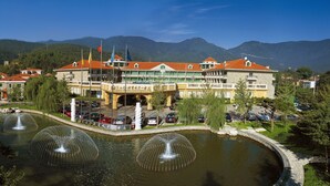 Un hotel con un edificio grande, varias banderas, una fuente y montañas al fondo.