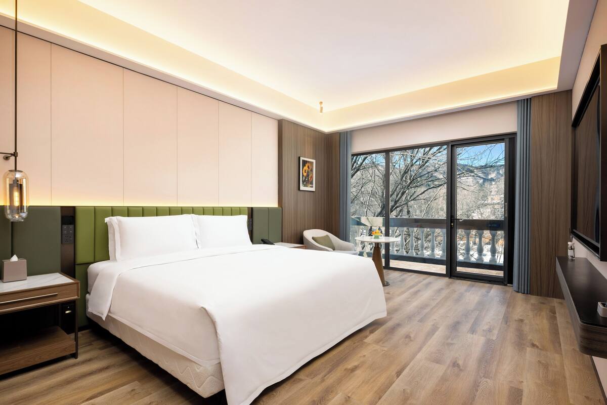 Une chambre d’hôtel avec un grand lit, un bureau, une chaise, une petite table et un balcon avec vue.