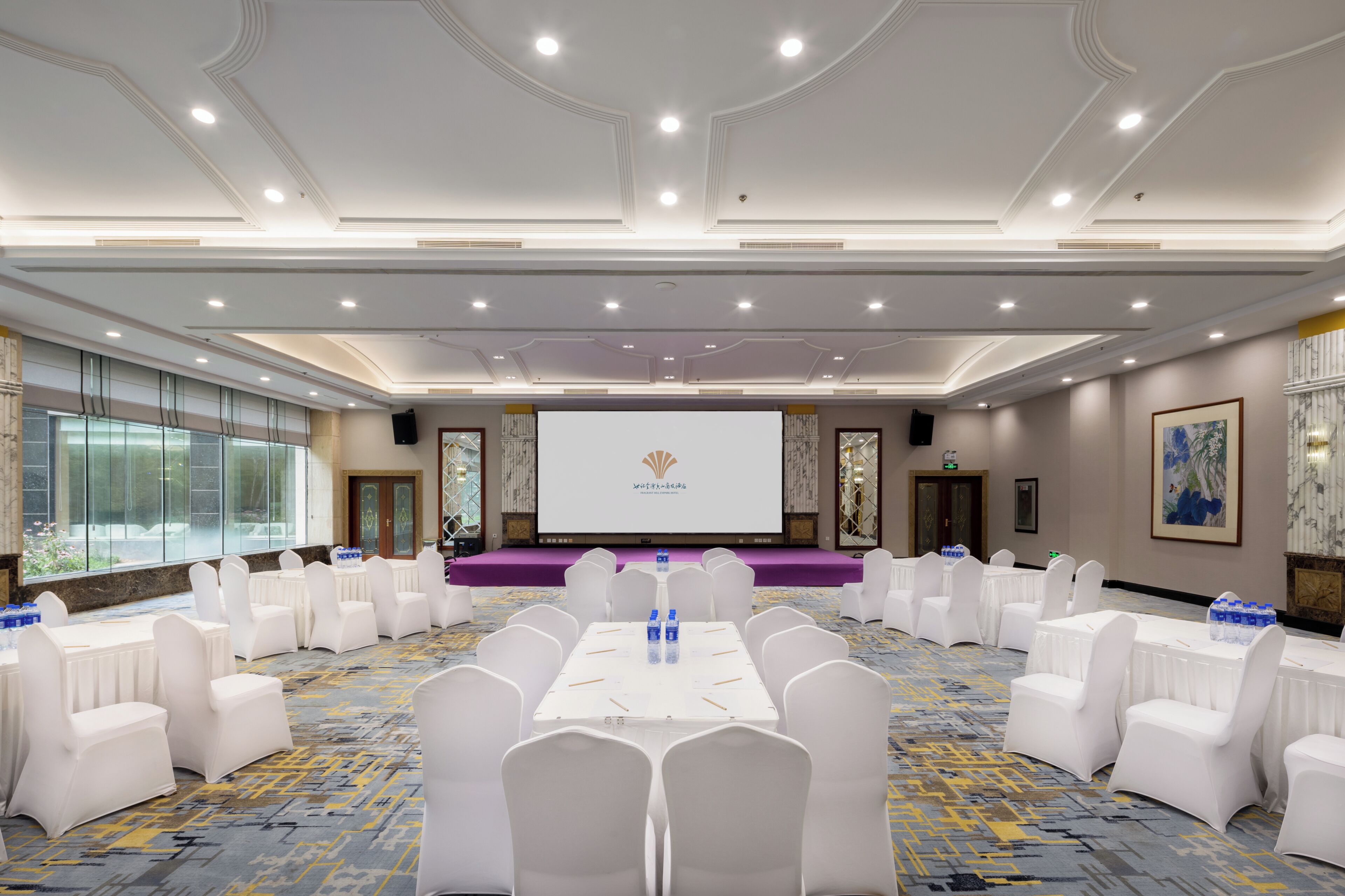 A conference room with a stage, white chairs, and a large screen.
