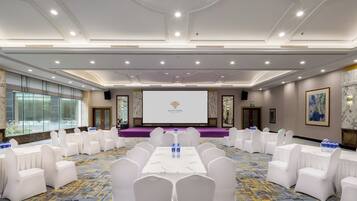 A conference room with a stage, white chairs, and a large screen.