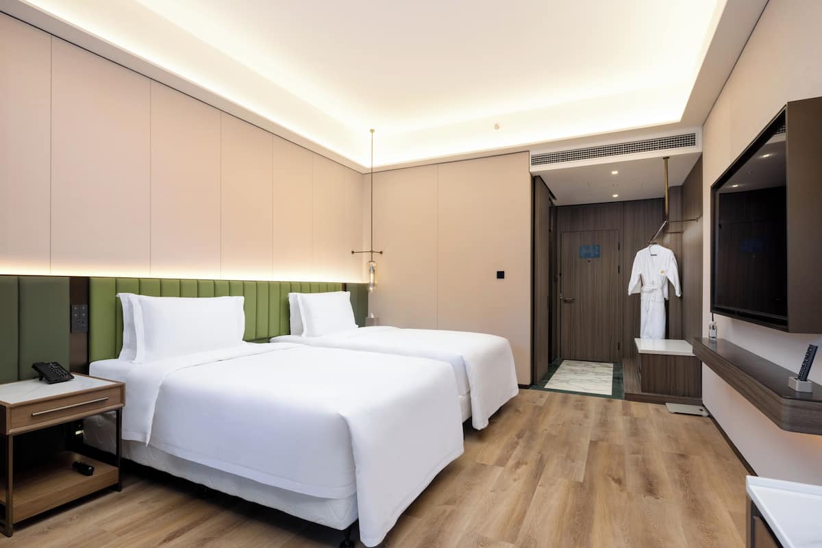 Une chambre d’hôtel avec deux lits, une table de chevet avec un téléphone, une télévision et une robe accrochée au mur.