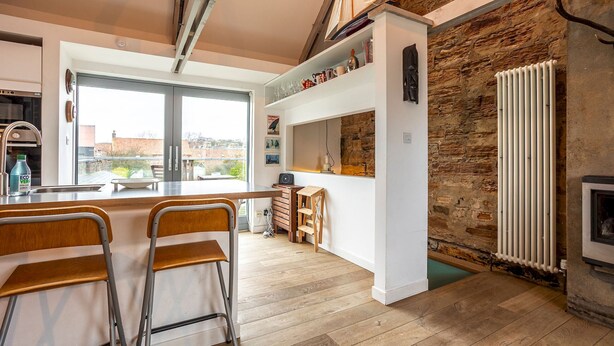 Una cucina moderna con parete in pietra, sgabelli da bar in legno e vista panoramica attraverso ampie finestre.