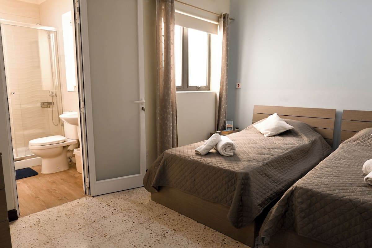 A bedroom with two beds, a window, a shower, and a toilet.