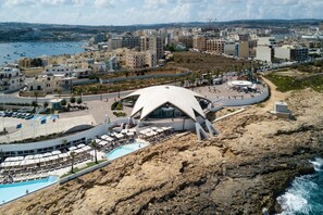 A coastal hotel with a unique white dome structure, a pool, and a view of the sea and cityscape. - Cozy Ensuite Rooms (St. Paul's Bay)
