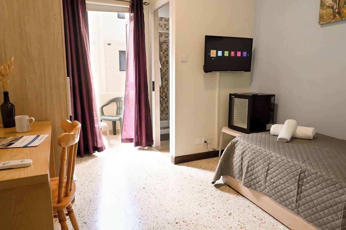 A hotel room with a bed, a television, a desk with a chair, and a window with curtains.