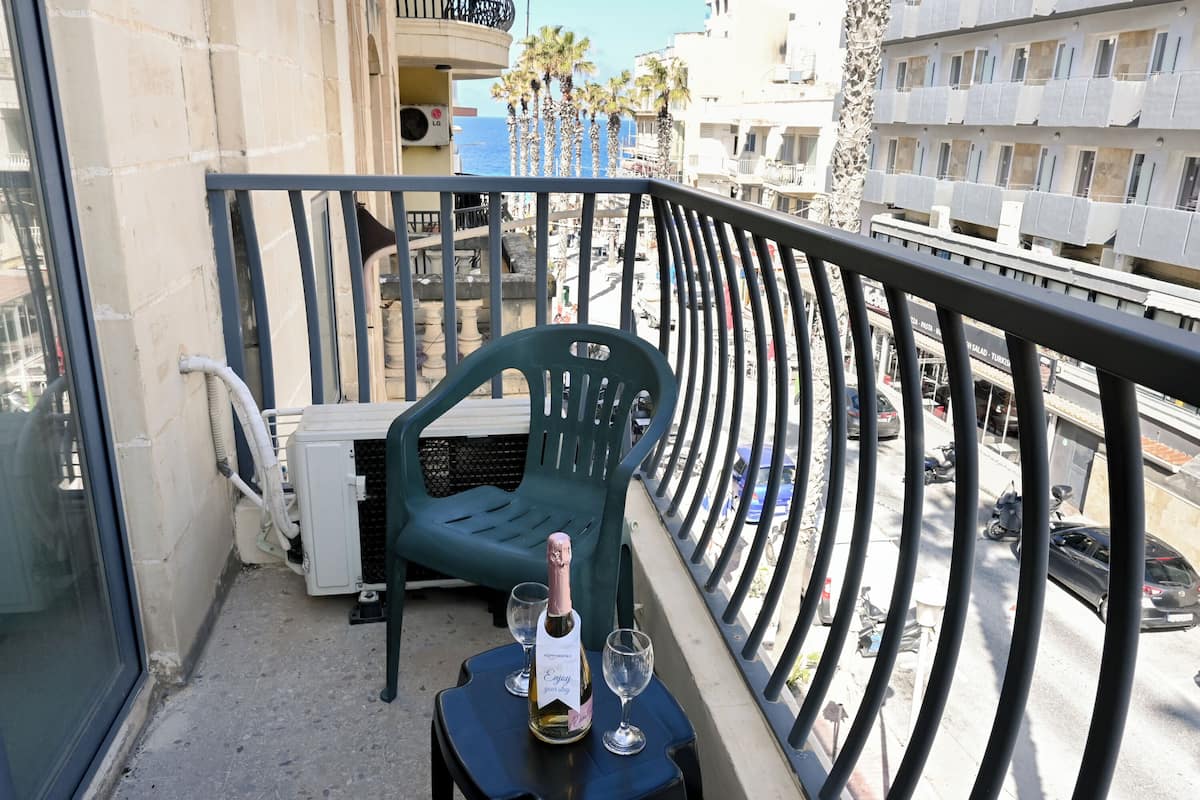 A balcony with a table, a chair, a bottle of champagne, and two glasses.