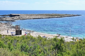 Une plage côtière bordée de formations rocheuses, aux eaux d’un bleu limpide et à la végétation clairsemée.