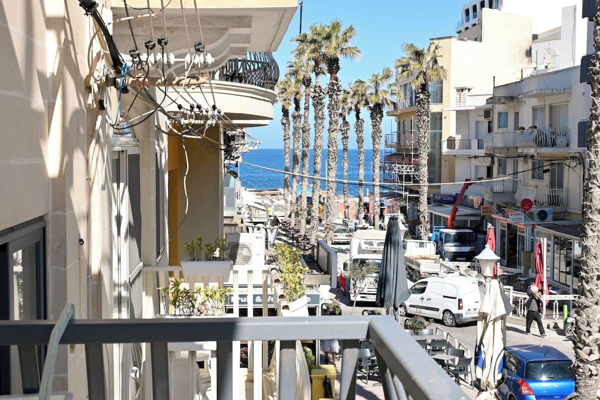 A balcony with a view of the street, palm trees, and a building with visible balconies and windows.