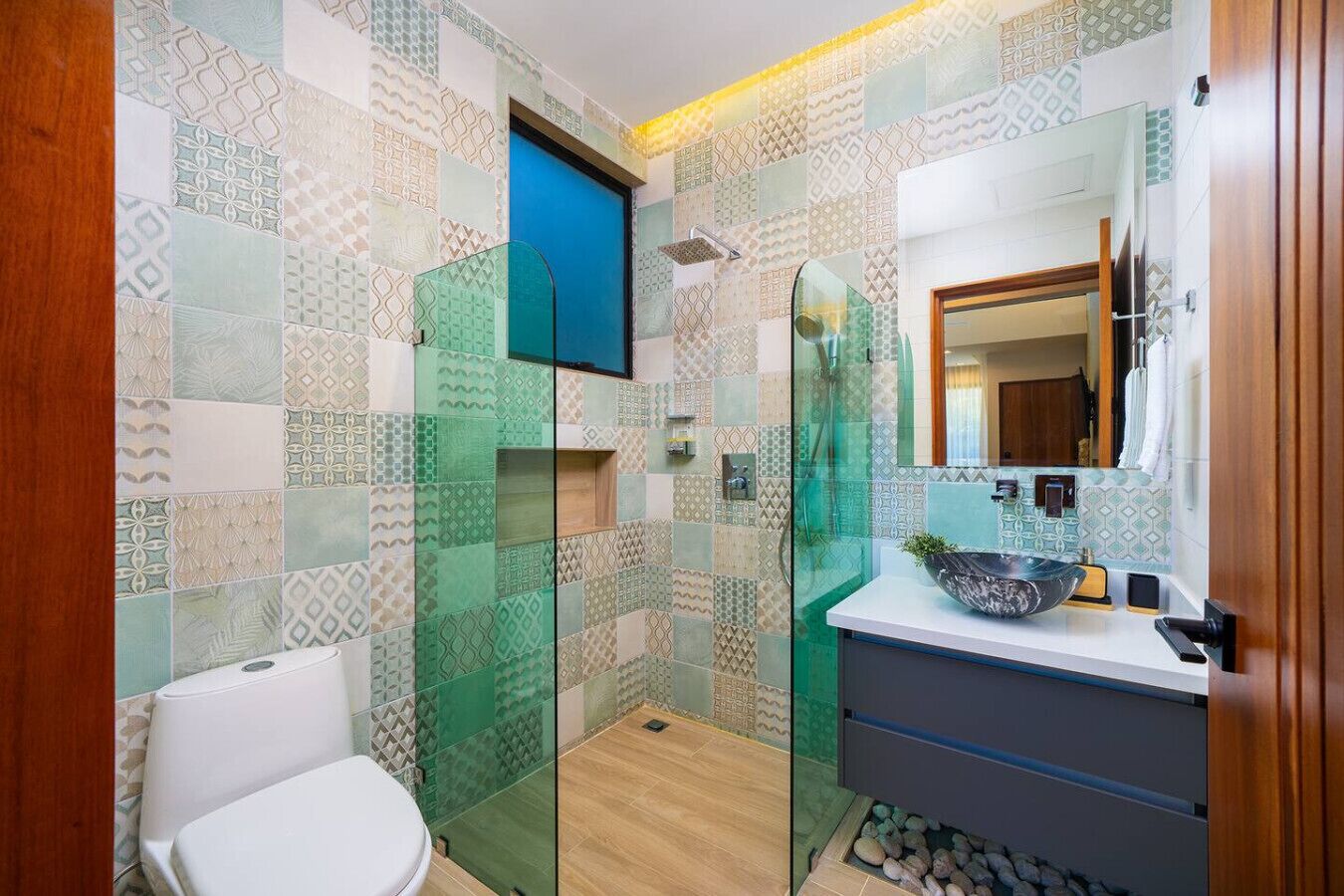 A bathroom with patterned tiles, a glass shower enclosure, a white toilet, and a sink with a bowl.