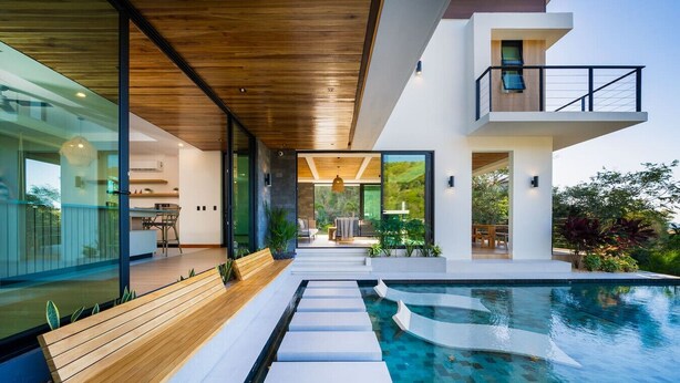 Een modern huis met zwembad, houten terras en glazen wanden.