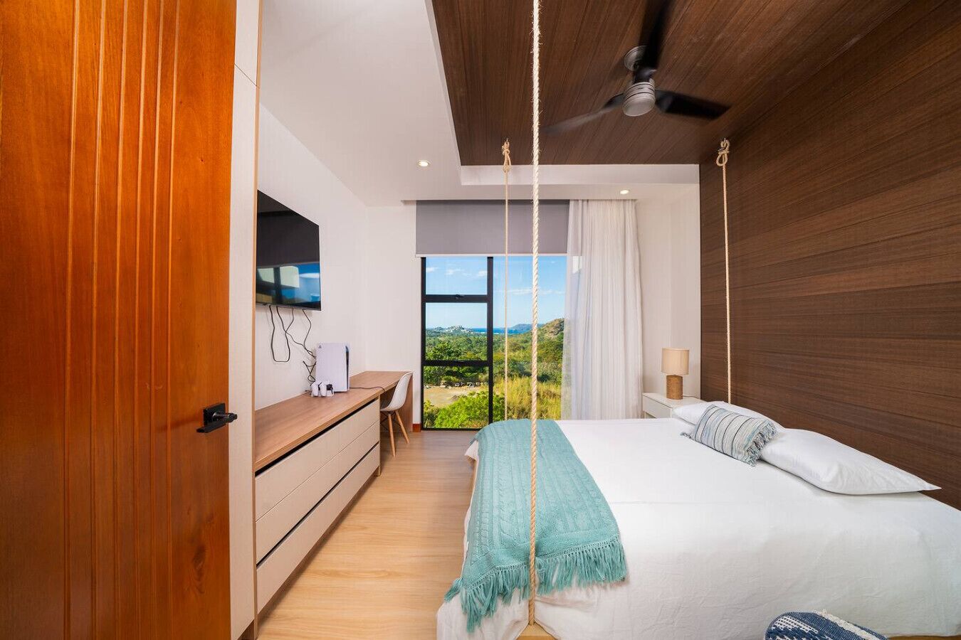 Ein Schlafzimmer mit Bett, Schreibtisch, Fernseher und Blick ins Freie.