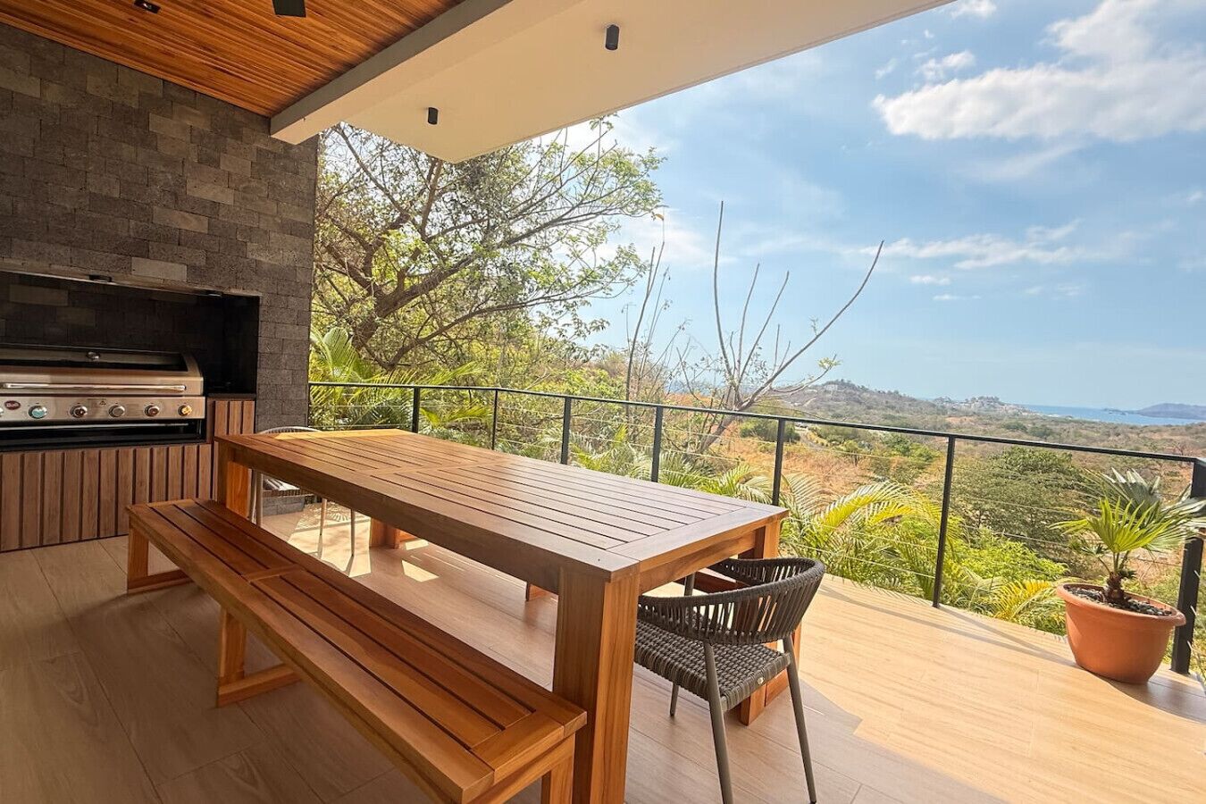 Cocina al aire libre con una parrilla, una mesa de madera y un banco, con vistas a un paisaje pintoresco.