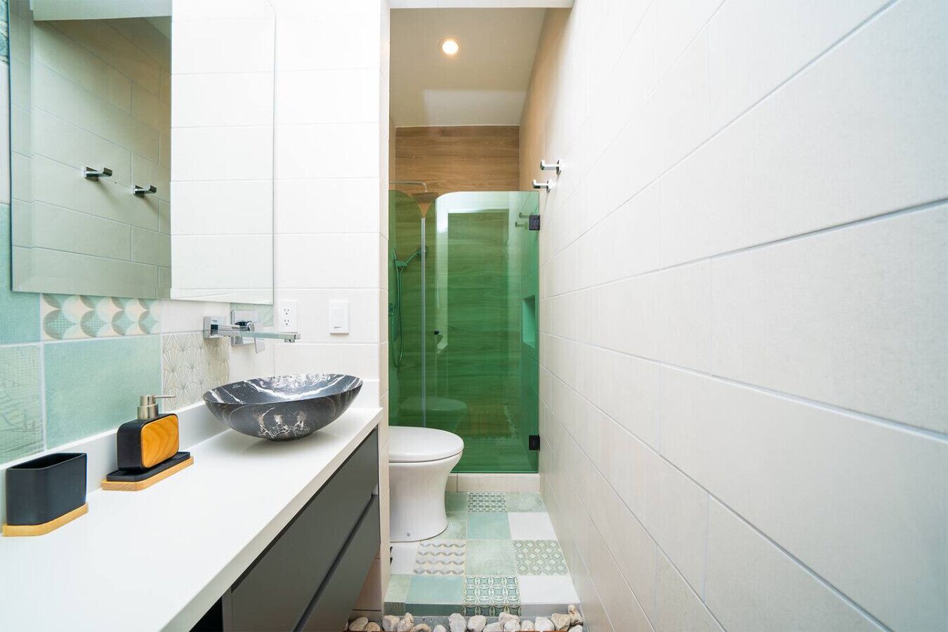 A bathroom with a white sink, a black and white bowl, a toilet, and a glass shower enclosure.