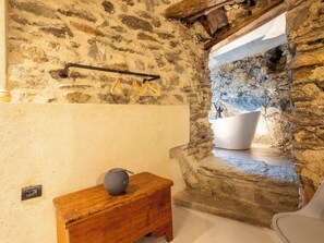 Ein Badezimmer mit Steinwänden, einer Badewanne, einer hölzernen Sitzbank und einem hängenden Handtuchhalter.