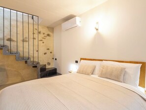 A hotel room with a bed, a wooden headboard, a wall-mounted air conditioner, a light fixture, and a unique textured wall with a staircase. - Beautiful apartment for 4 people with A/C, WIFI, TV and balcony (Morbegno)