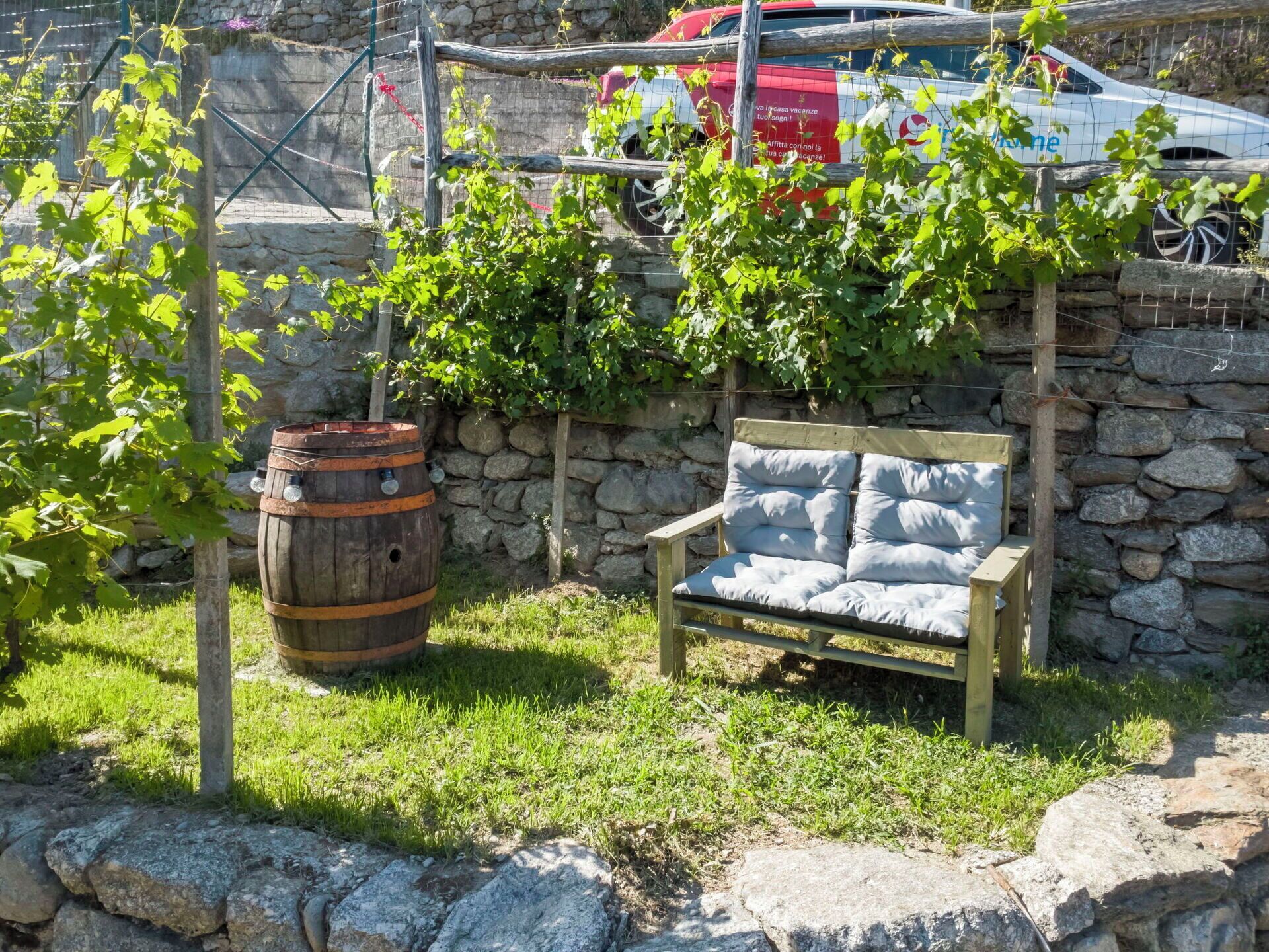Un espacio de estar al aire libre rústico, con un muro de piedra, un barril de madera y un banco.
