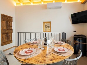 A round wooden dining table with woven placemats, a bottle of wine, and multiple glasses. - Beautiful apartment for 4 people with A/C, WIFI, TV and balcony (Morbegno)