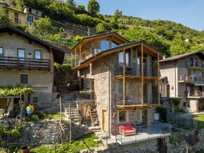 Un bâtiment en pierre à plusieurs étages, doté de balcons, d’un escalier et d’un petit espace extérieur aménagé pour s’asseoir.