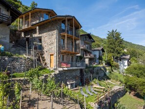Ein mehrstöckiges Steinhaus mit Balkonen, einer Steintreppe und einem Weinberg.
