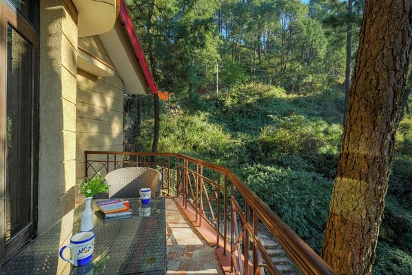 Un balcon avec une table, un vase et une chaise, donnant sur une zone boisée.