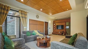 A living room with a wooden ceiling, a sofa set, a coffee table, and a TV. - Alaya Stays 3BHK Golden Meadow Villa (Kasauli)
