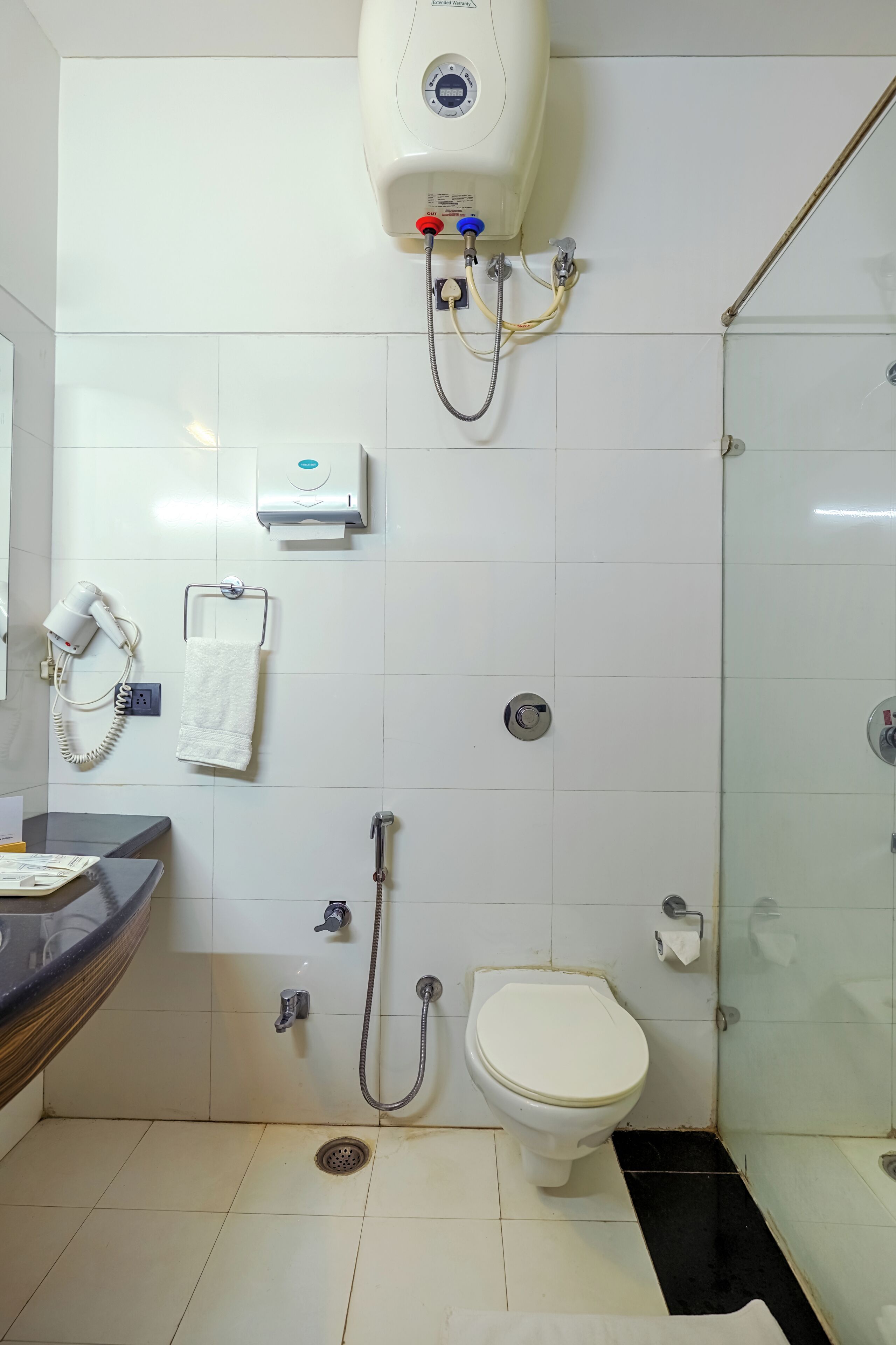 A bathroom with a toilet, shower, and a hairdryer on the wall.