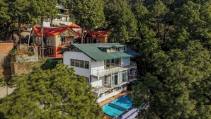 A multi-story building with a swimming pool, surrounded by dense forest. - Alaya Stays 3BHK Golden Meadow Villa (Kasauli)