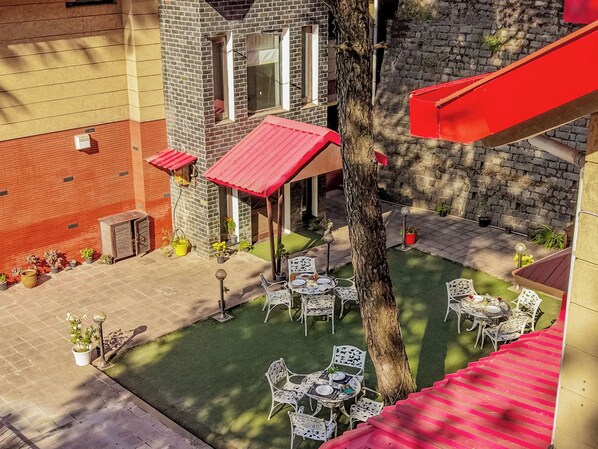 A courtyard with outdoor seating, a tree, and a building with a red roof. - Alaya Stays 3BHK Golden Meadow Villa (Kasauli)