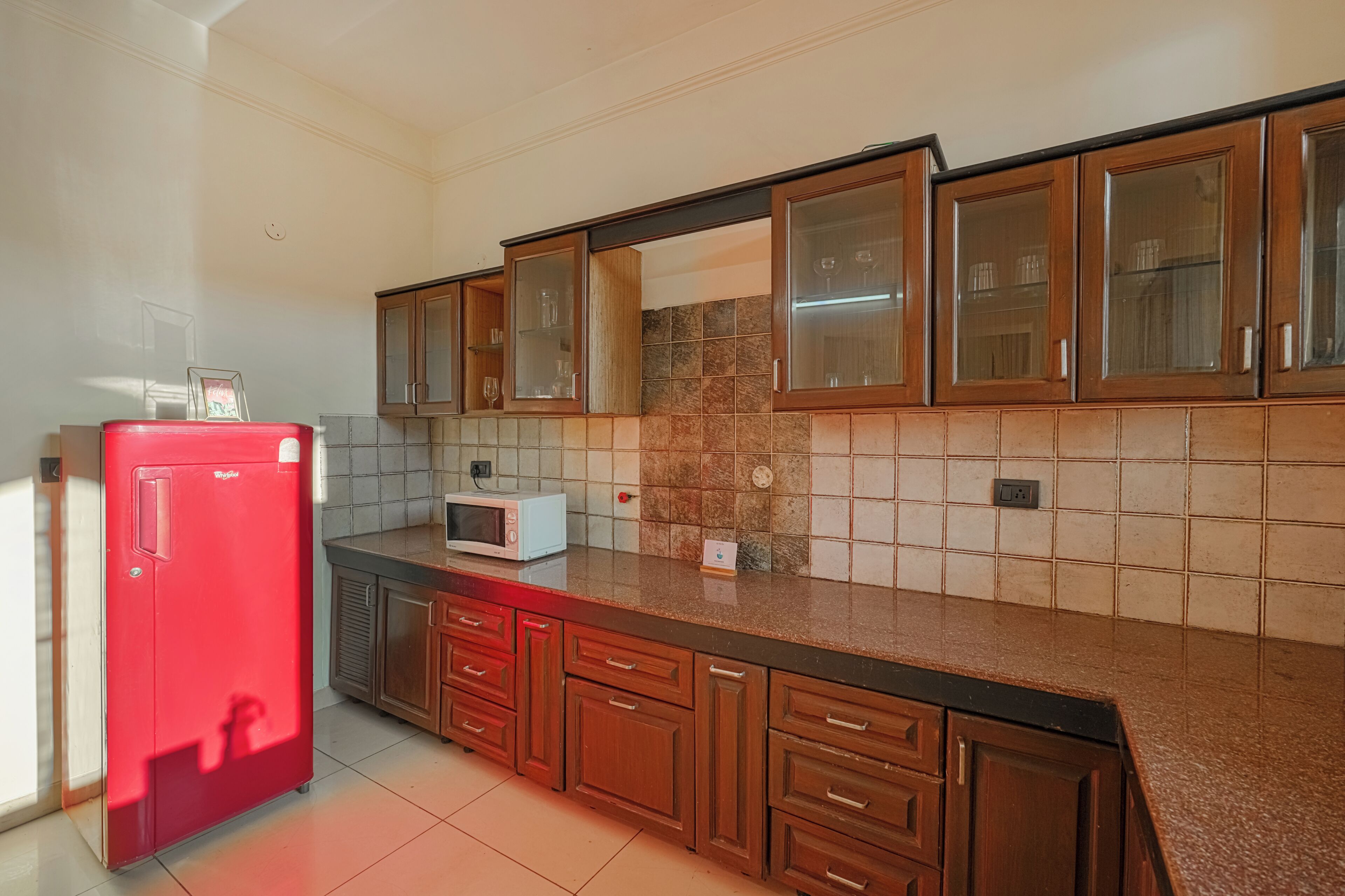 A kitchen with wooden cabinets, a red refrigerator, a microwave, and tiled backsplash.