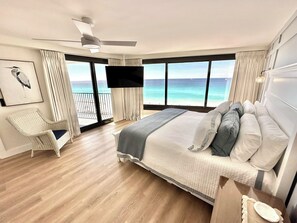 Ein Schlafzimmer mit Bett, Stuhl, Deckenventilator, Fernseher und einem Balkon mit Meerblick.