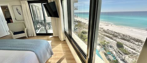 A hotel room with a large bed, a TV, and a balcony with a beach view.
