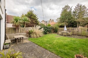 Ein Garten mit Holzzaun, einem Patio-Tisch und -Stühlen sowie einem Rasen.