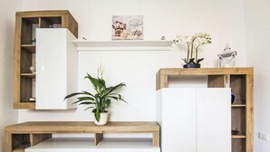 Uma sala de estar moderna com um móvel embutido branco para entretenimento, prateleiras de madeira, um banco branco e um vaso com planta.