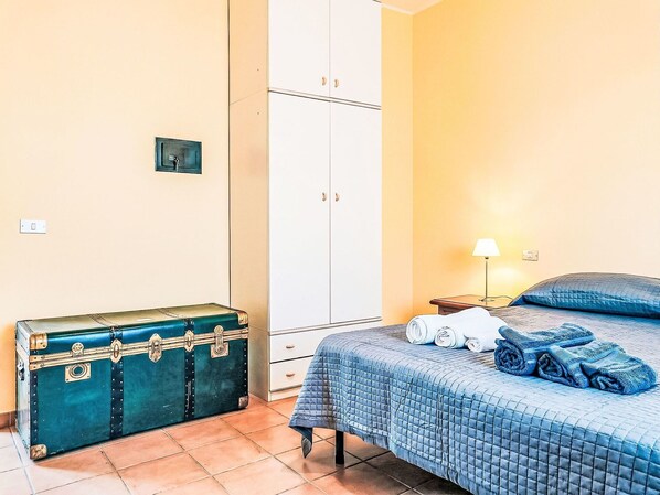 A bedroom with a bed, a suitcase, a wardrobe, and a nightstand with a lamp.
