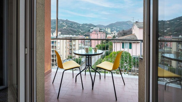 Ein Balkon mit Tisch und Stühlen, eine Glastür und Blick auf Gebäude und Hügel.
