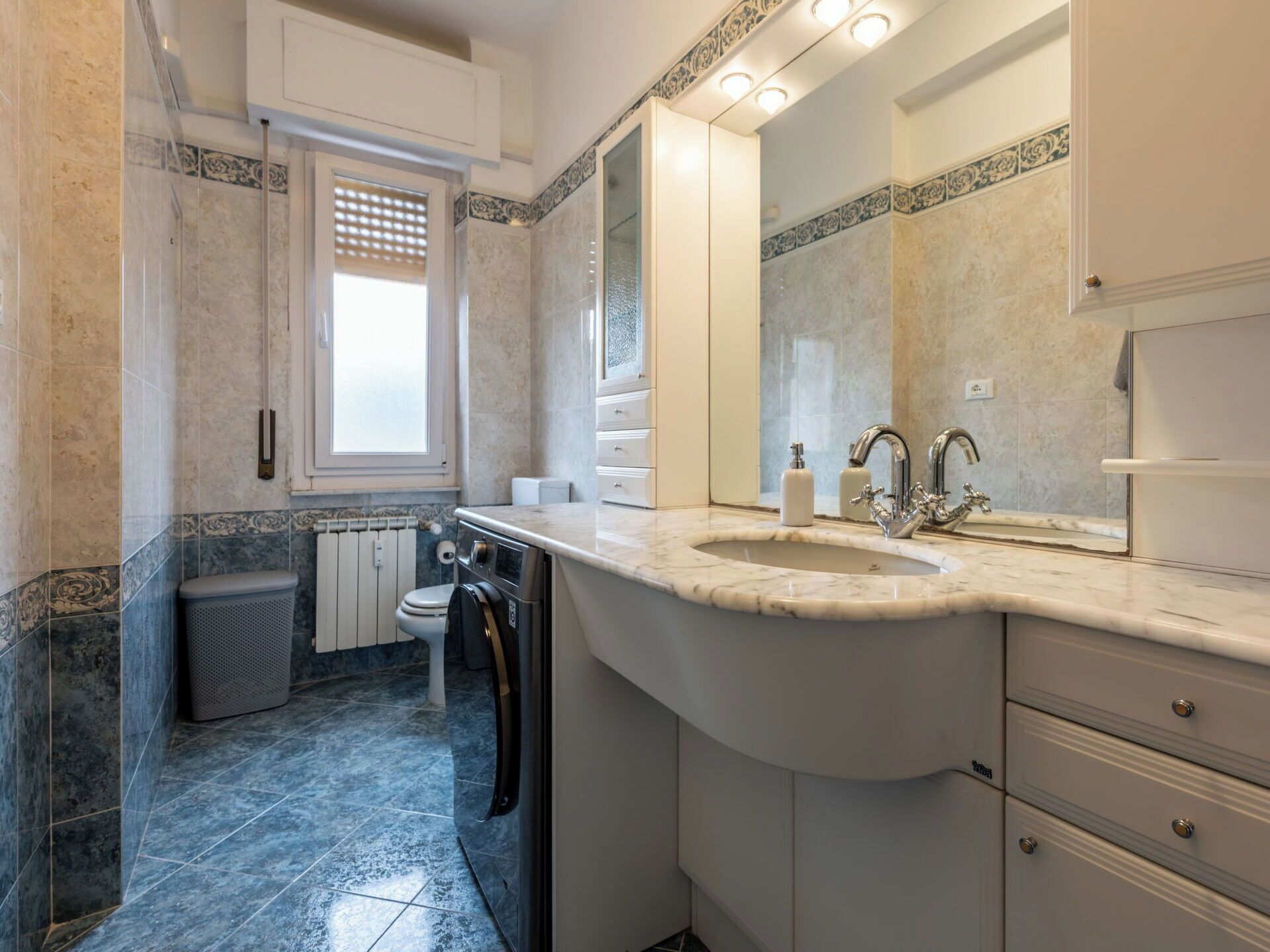Ein Badezimmer mit einem großen Waschbecken, einem Spiegel, einer Toilette und einem Fenster.