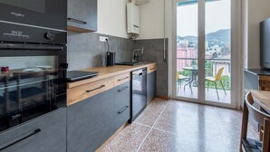 Eine moderne Küche mit Einbauofen, Kaffeemaschine und Geschirrspüler. Ein Balkon bietet Blick auf die Stadt und die Berge.