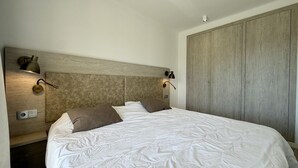 Ein Schlafzimmer mit einem großen Bett, zwei Wandleuchten, einem Holzschrank und einem Schalter am Wand.