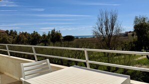 Ein Balkon mit weißer Brüstung, einem weißen Stuhl und Blick auf eine Küstenlandschaft mit Bäumen und Gebäuden.